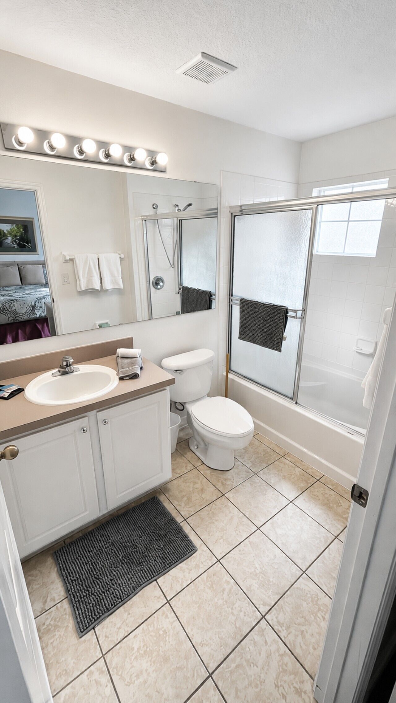 A bathroom with a vanity, sink, mirror, toilet, shower, and a tiled floor.