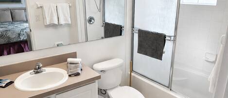 A bathroom with a vanity, sink, mirror, toilet, shower, and a tiled floor.