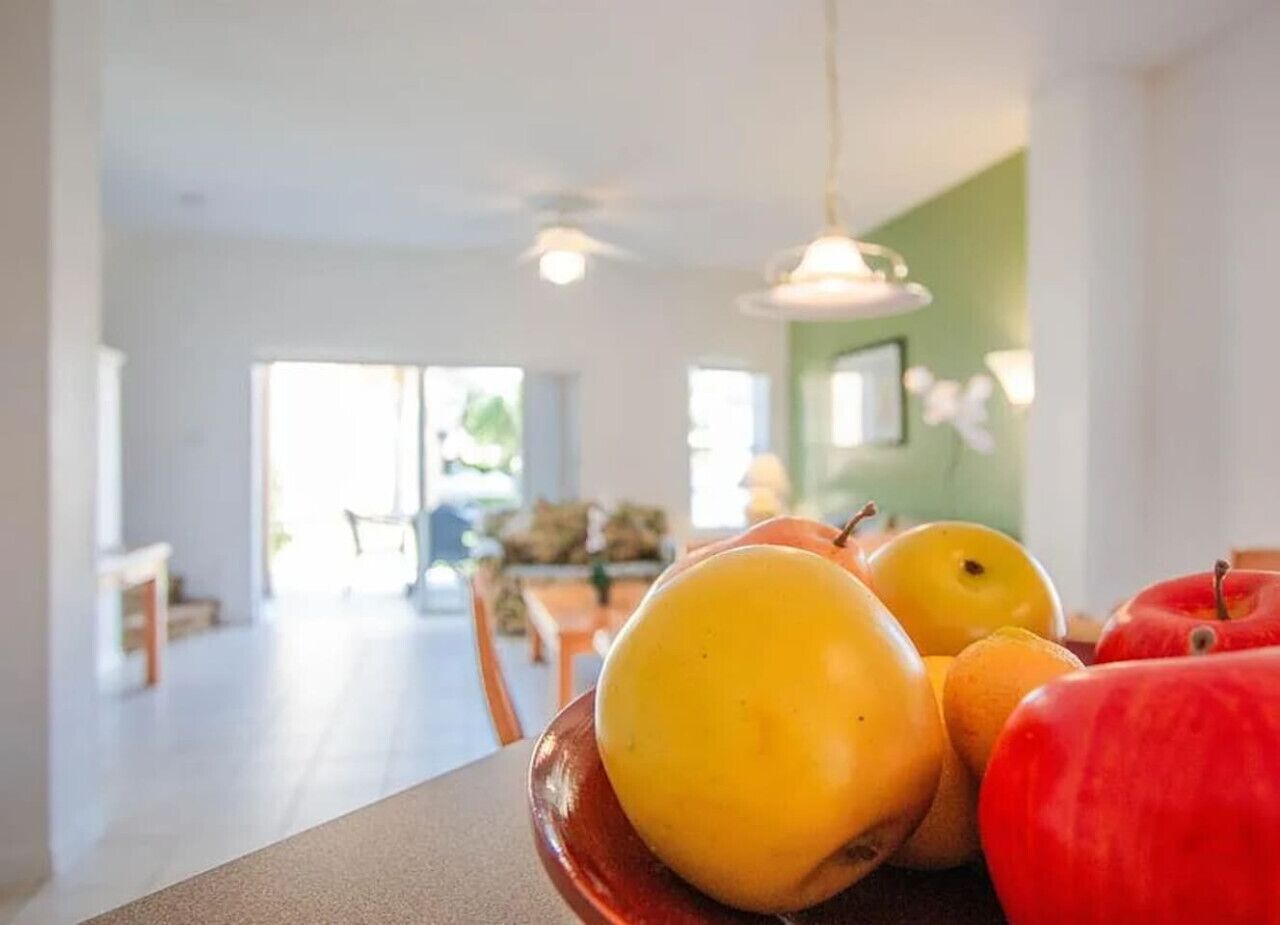 A dining area with a table set for two, featuring a fruit bowl with apples and oranges.