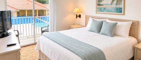 A hotel room with a bed, a TV, a desk, a lamp, and a painting of a beach.