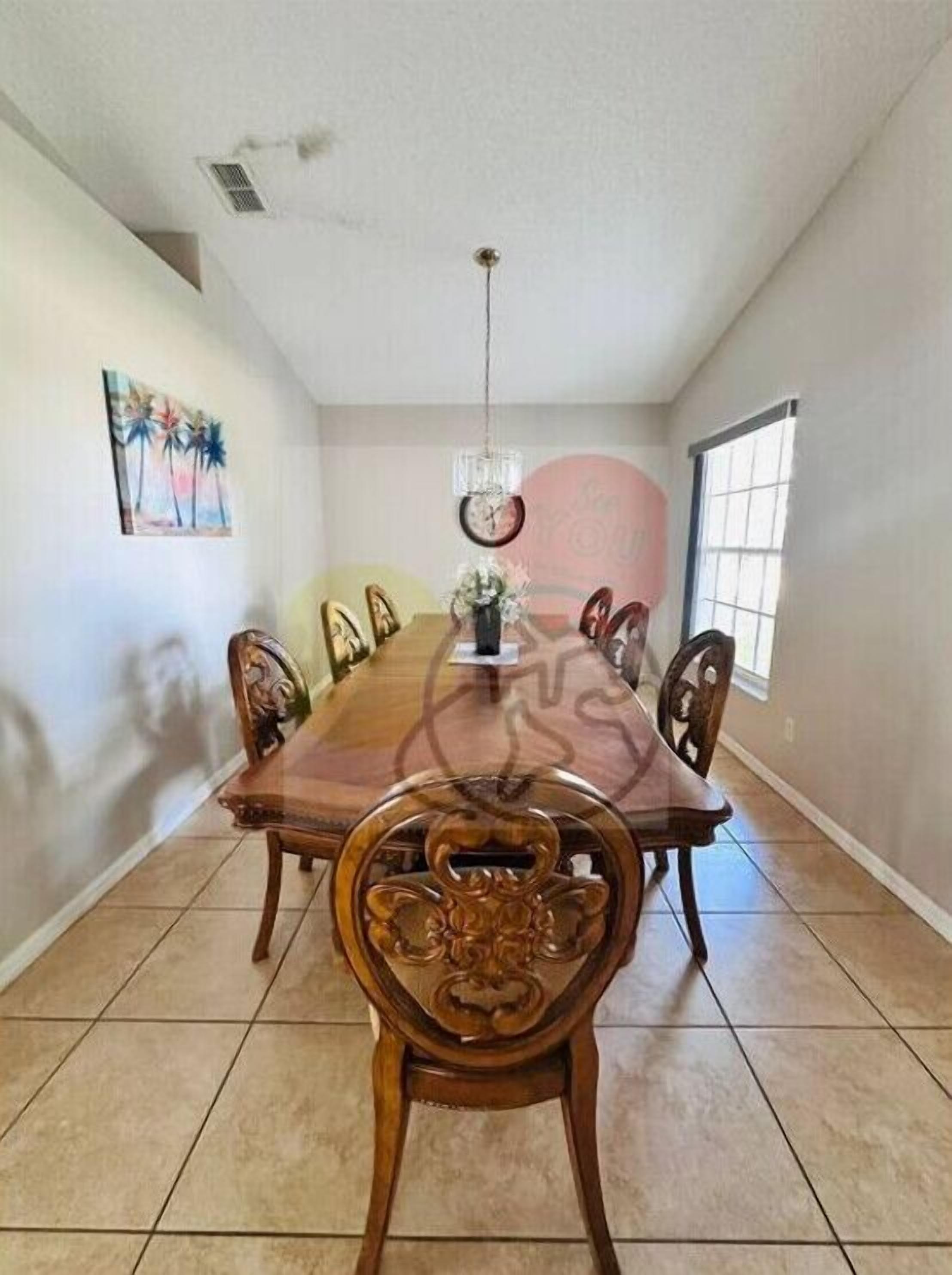 Une salle à manger avec une grande table en bois, six chaises, un lustre, une horloge et une fenêtre.