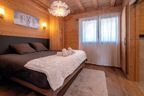 A wooden cabin bedroom with a bed, a painting, a light fixture, and a window with curtains. - Chalet 14p - Jacuzzi - Lift - Sport - 300m from the slopes - Centre les 2 Alpes (Les Deux Alpes)