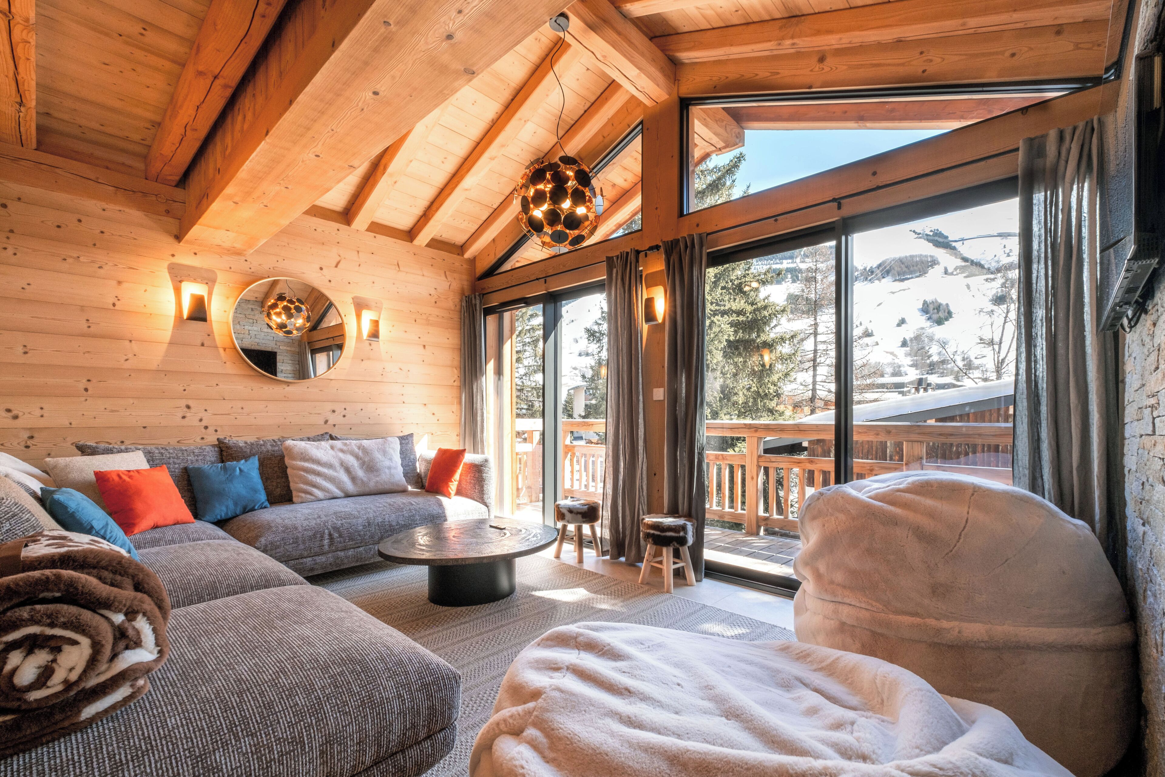Ein gemütliches Blockhaus-Interieur mit einer Couch, einem runden Couchtisch und einem großen Fenster mit Blick ins Freie.