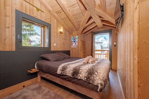 A wooden cabin bedroom with a bed, a window, a poster, and a door leading outside. - Chalet 14p - Jacuzzi - Lift - Sport - 300m from the slopes - Centre les 2 Alpes (Les Deux Alpes)