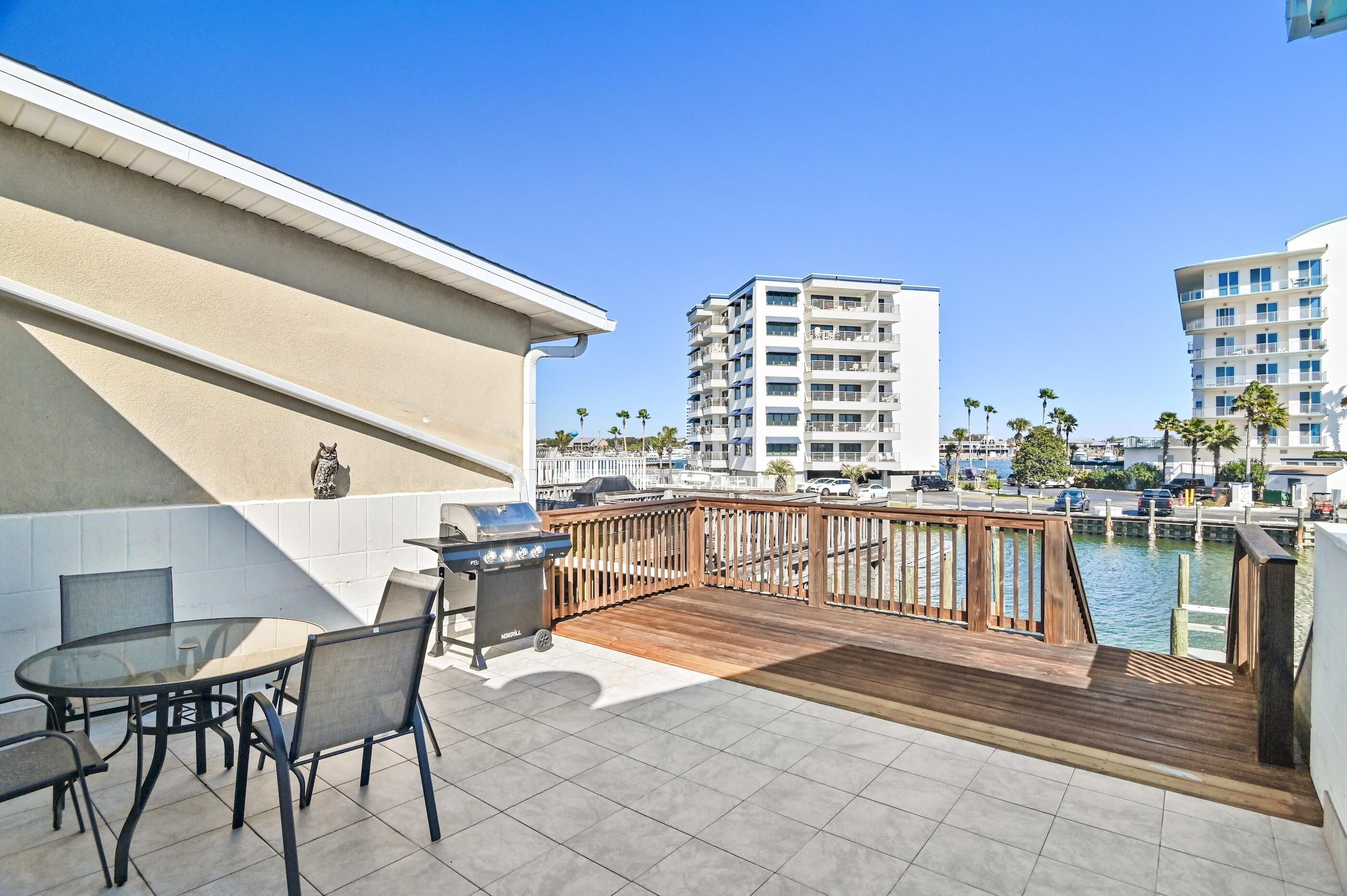A rooftop patio with a view of a marina, featuring a wooden deck, outdoor seating, and a grill.