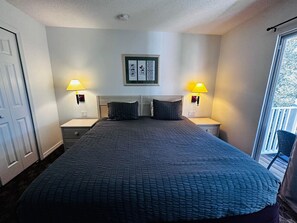 Ein Schlafzimmer mit einem großen Bett, zwei Nachttischlampen, einem gerahmten Bild an der Wand und einem Fenster mit Blick ins Freie.