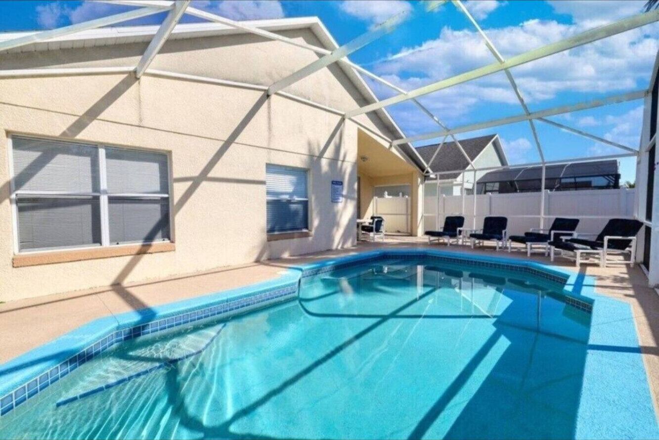 Et poolområde med en klar blå pool, liggestole og en overdækket terrasse.