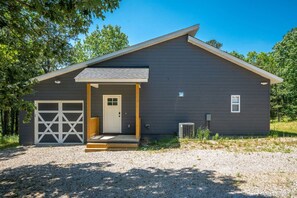 Un bâtiment moderne de plain-pied, à l’extérieur sombre, doté d’un garage et d’un porche à l’avant.