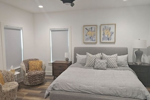 Une chambre avec un grand lit, deux tables de chevet, une chaise et deux fenêtres.