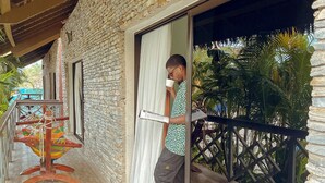 A stone building with a wooden balcony, a hammock, and a person standing by a window. - Comoé Lodge Hôtel Resort & Spa (Ekressinville)