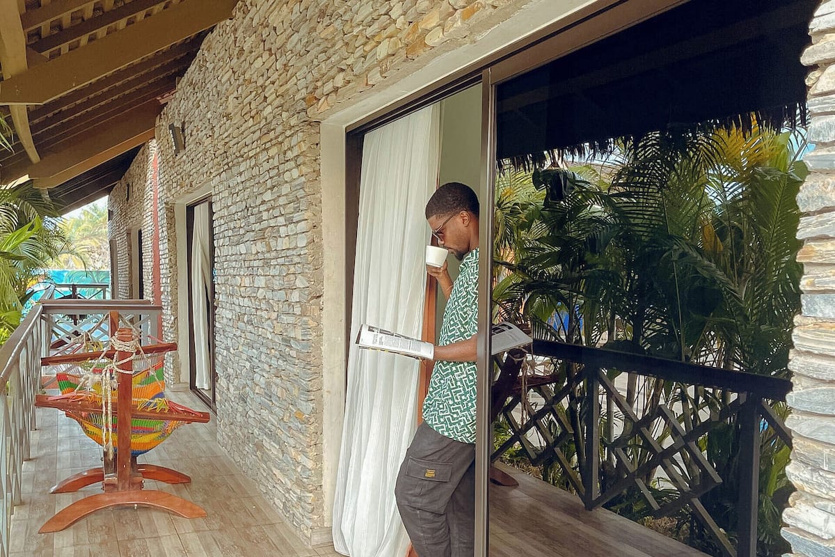 A stone building with a wooden balcony, a hammock, and a person standing by a window.