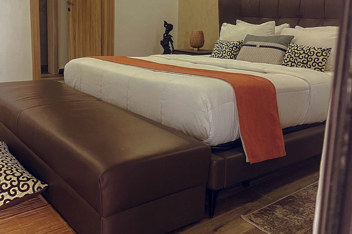 A bedroom with a large bed, a wooden door, and a framed artwork on the wall.