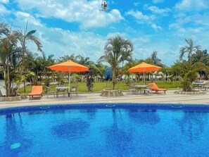 Zona de piscina con sombrillas naranjas, sillas de descanso y palmeras.