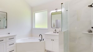 Ein modernes Badezimmer mit einer Badewanne, einer Dusche, einem Waschtisch mit Spiegel und einem Fenster.