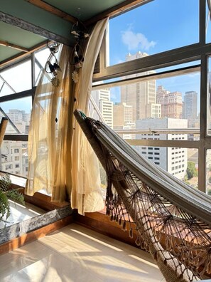 A hammock in a room with large windows overlooking a cityscape. - Java Themed Loft. With a spectacular view. (São Paulo)