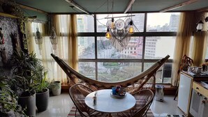 Een gezellige kamer met een hangstoel, een ronde tafel en een uitzicht op de stad door grote ramen.
