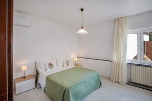 Un dormitorio con cama, lámparas de noche, una lámpara colgante, una ventana con cortinas y un radiador.