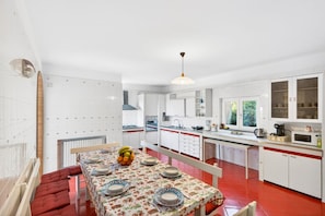 Una cocina moderna con armarios blancos, una mesa de comedor dispuesta con platos y un frutero, y suelo rojo.