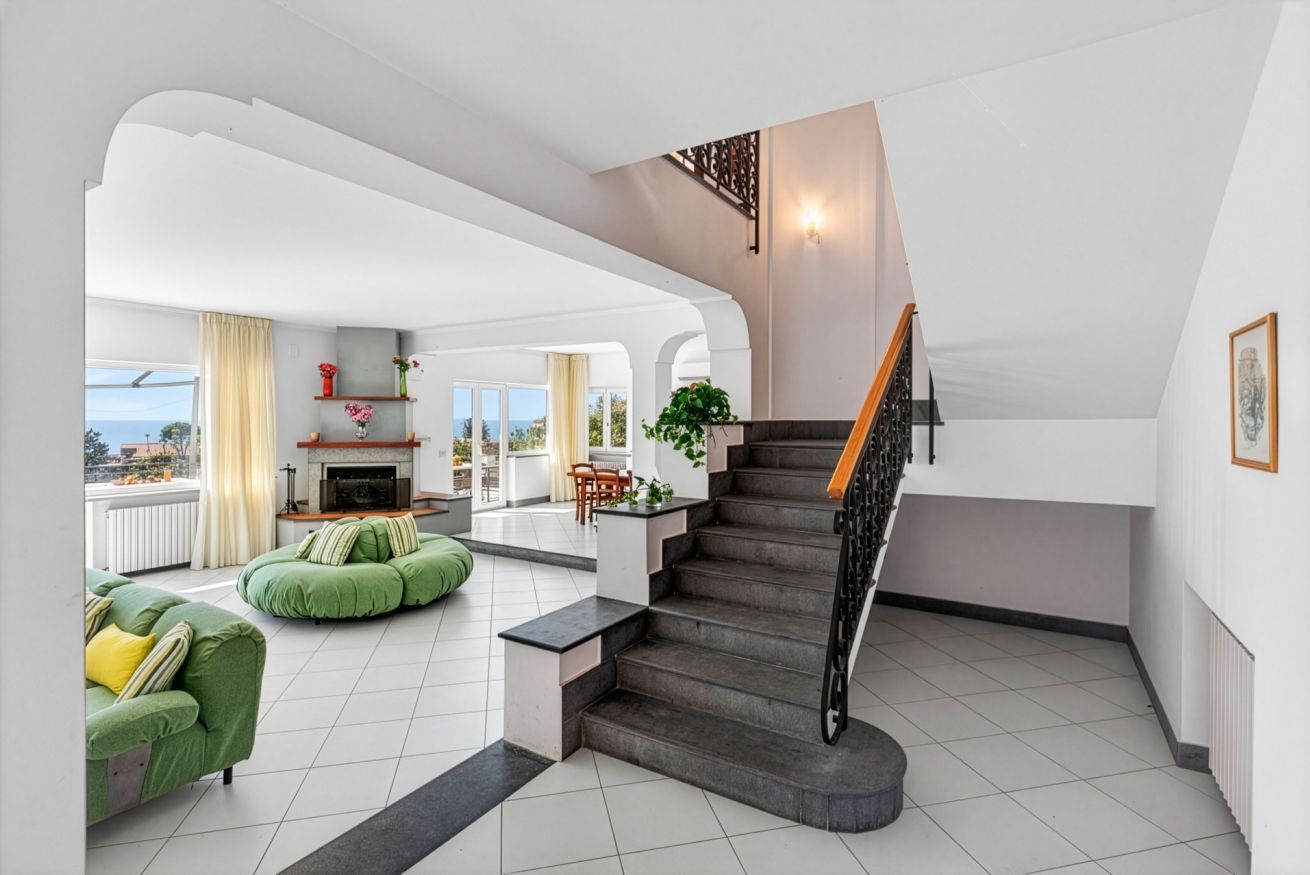 A spacious living area with a staircase, green seating, and a view of the outdoors.