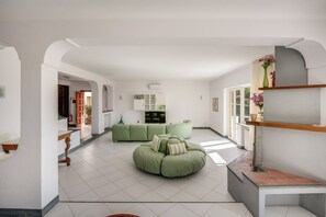 Ein geräumiger Wohnbereich mit einem grünen Ecksofa, einem Flachbildfernseher und einem Bücherregal.