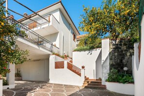 A white building with a balcony, a stone wall, and a tiled courtyard. - SorrentoVibes - The Lemon Grove Villa with private pool, garden and terrace (Massa Lubrense)