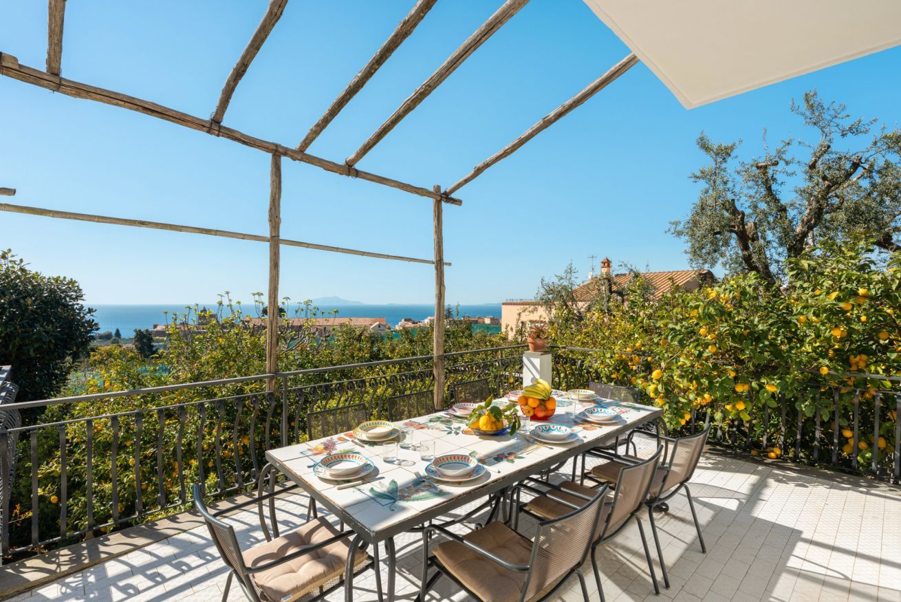 A terrace with a table set for dining, overlooking a scenic view with trees and a distant landscape.