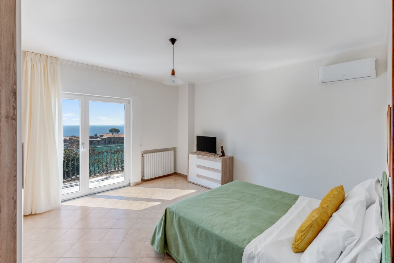 A bedroom with a bed, a TV, a radiator, and a view of the outside.