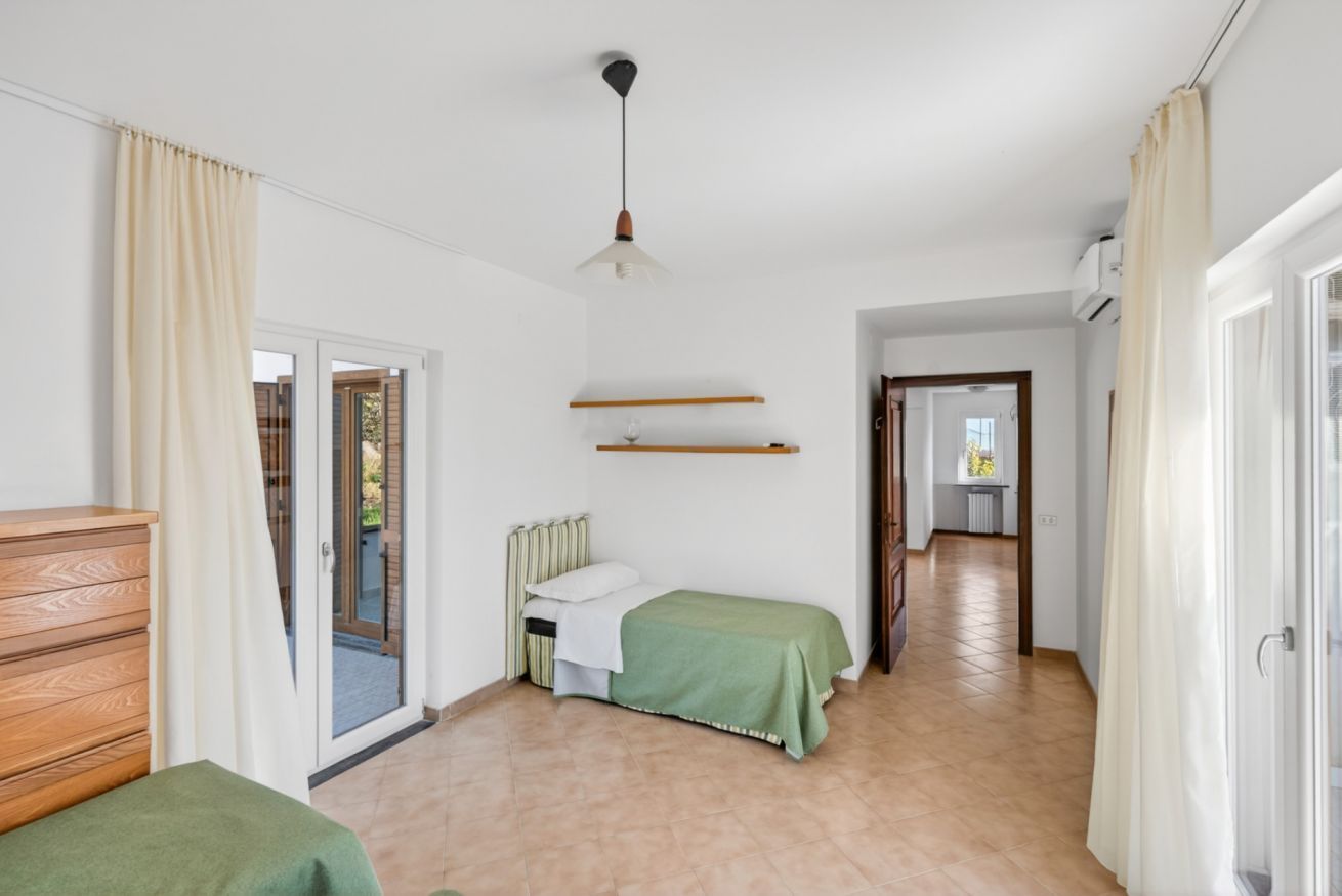 A room with a bed, a wooden dresser, a hanging light fixture, and a sliding glass door leading to an outdoor area.