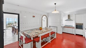 Una cocina con armarios blancos, suelo de baldosas rojas y una zona de comedor con mesa preparada para cuatro.