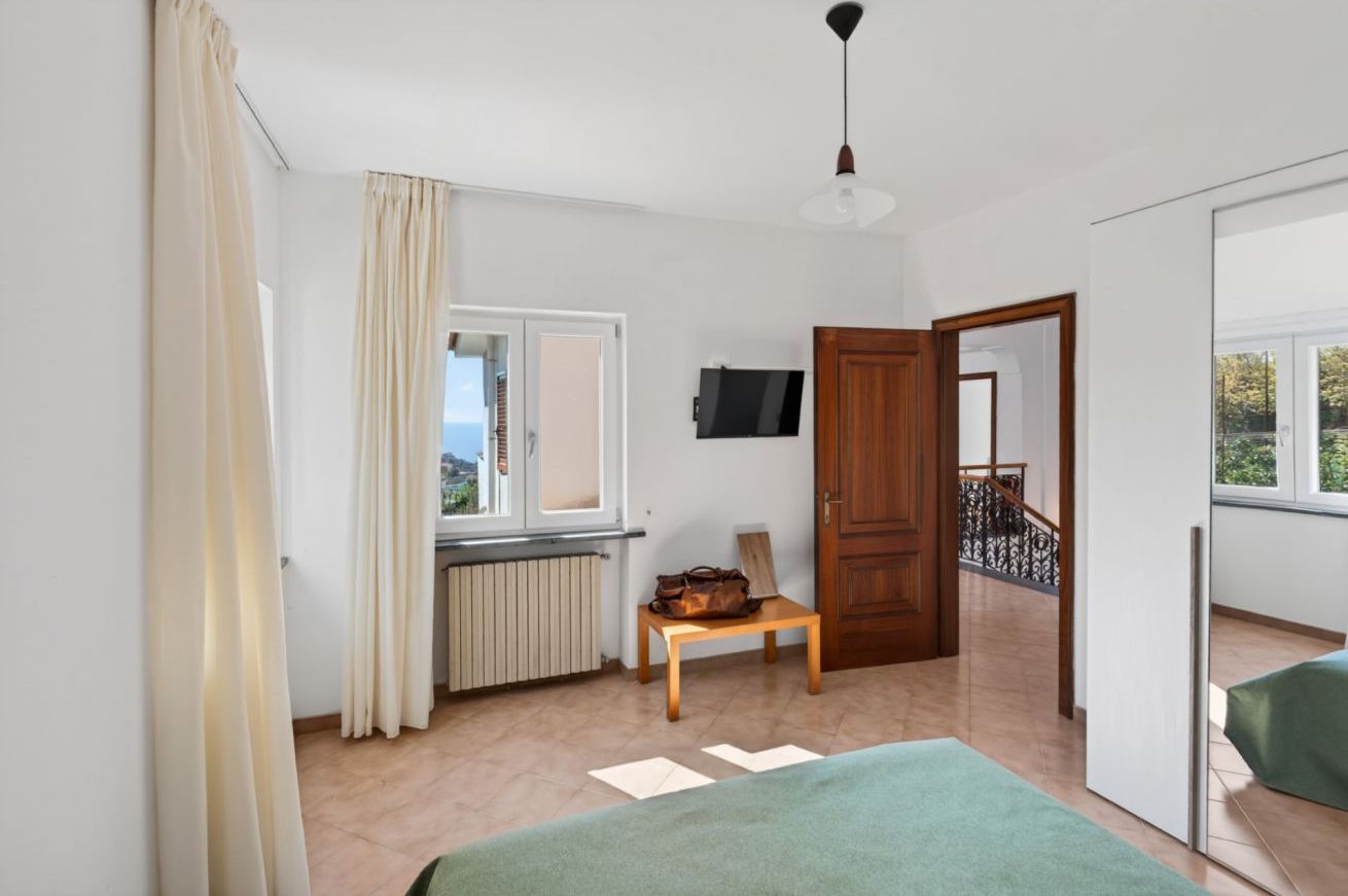 Ein Zimmer mit einem Bett, einem Tisch mit einer Tasche, einem Fernseher, einem Fenster und einer Tür, die auf einen Balkon führt.