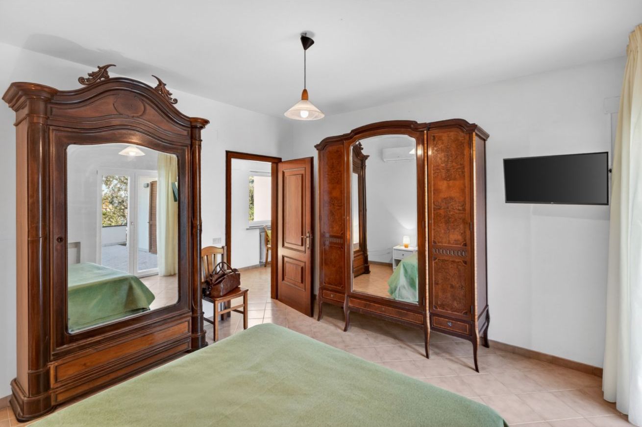 A bedroom with a large mirror, a bed, a wardrobe, and a television.