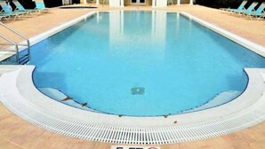 Una piscina rectangular con un bordeado de baldosas, una estructura cubierta con techo rojo y sillones de descanso alrededor de la piscina.
