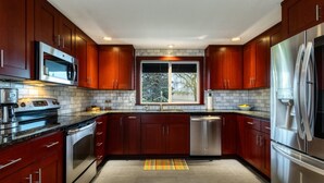 Une cuisine moderne avec des meubles en bois foncé, des appareils électroménagers en acier inoxydable et une grande fenêtre qui laisse entrer la lumière naturelle.