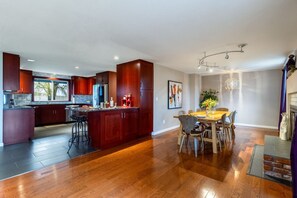 Une cuisine moderne avec des meubles de couleur bois foncé, un îlot central et un coin repas comprenant une table et des chaises en bois.