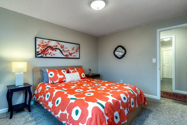 A bedroom with a large bed, a nightstand, a wall-mounted mirror, and a door leading to another room.
