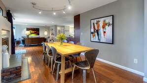 Un espace de repas moderne avec une table et des chaises en bois, un vase rempli de fleurs et un grand tableau abstrait accroché au mur.