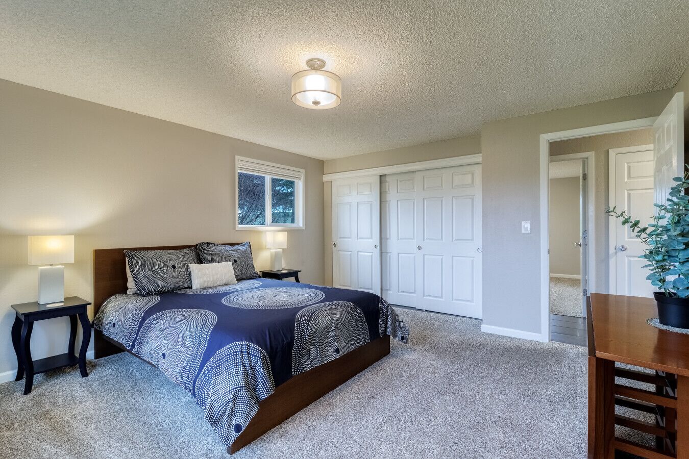 A bedroom with a large bed, two bedside tables with lamps, a ceiling light, a window, and a door.