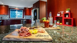 Une cuisine dotée de plans de travail en granit, d’une planche à découper en bois sur laquelle sont disposées des charcuteries, d’une bouteille de whisky et d’une étagère rouge.