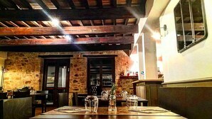 A restaurant with exposed wooden beams, stone walls, and a large dining table with chairs. - IL VECCHIO BRACIERE (San Venanzo)