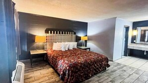 Ett hotellrum med en säng, sänglampor, ett litet bord, en spegel och ett element.