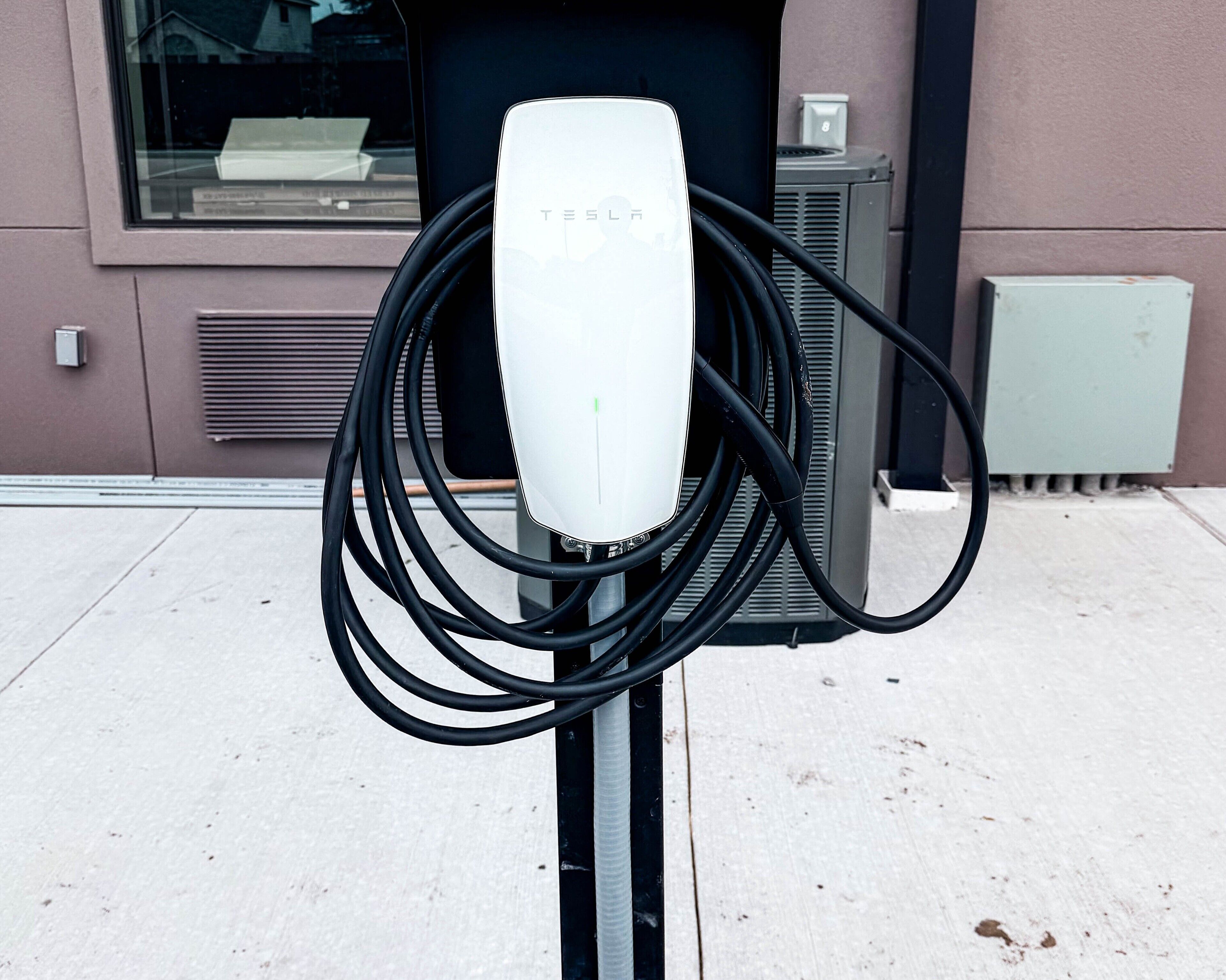 Une borne de recharge Tesla dotée de plusieurs câbles, située sur un trottoir devant un immeuble.