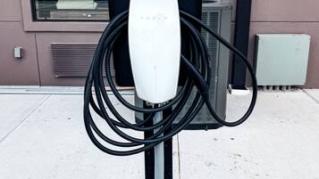 Une borne de recharge Tesla dotée de plusieurs câbles, située sur un trottoir devant un immeuble.