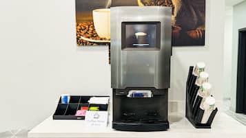 Una máquina de café con pantalla digital, una taza de café y un dispensador de granos de café sobre una encimera.