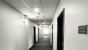 Un long couloir étroit, avec des portes de chaque côté, un sol recouvert de moquette et un plafond doté d’un éclairage encastré et de détecteurs de fumée.