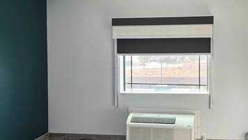 A room with a window, a white air conditioning unit, and a dark-colored wall.