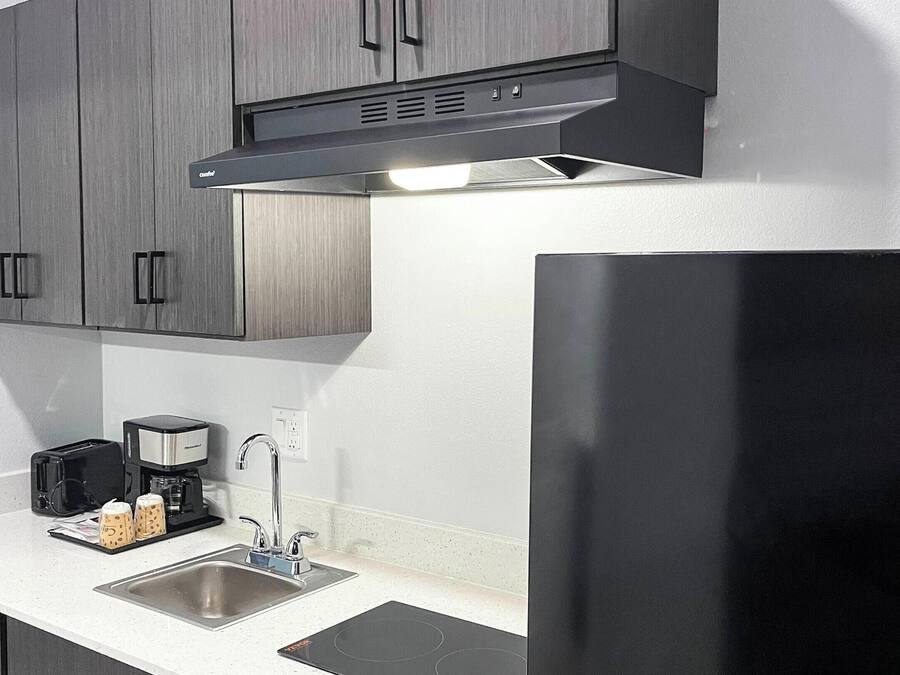 A modern kitchen with grey cabinets, a stainless steel sink, a coffee maker, and a black refrigerator.