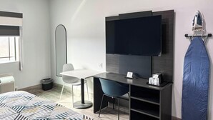 Una habitación de hotel moderna con una cama, un escritorio con silla, un televisor de pantalla plana y un tablero de planchar fijado a la pared.
