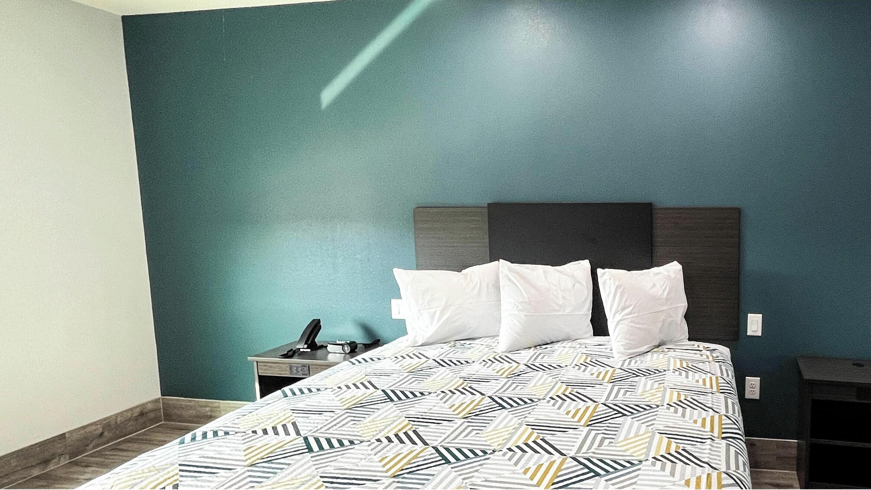 A neatly made bed with a patterned bedspread, a bedside table with a phone, and a wall with a teal color.