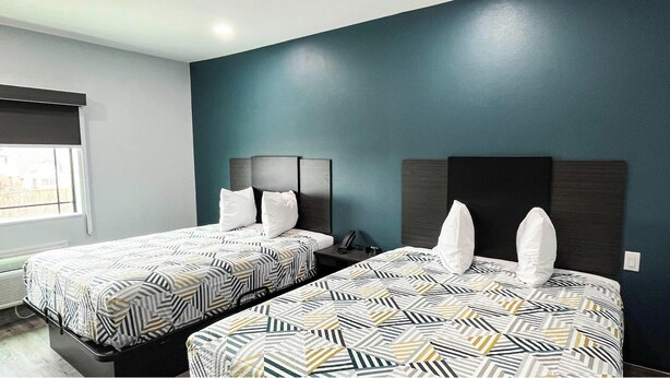 Una camera d'albergo con due letti, ognuno con biancheria a motivi decorativi e cuscini bianchi, affacciata su una parete color petrolio.