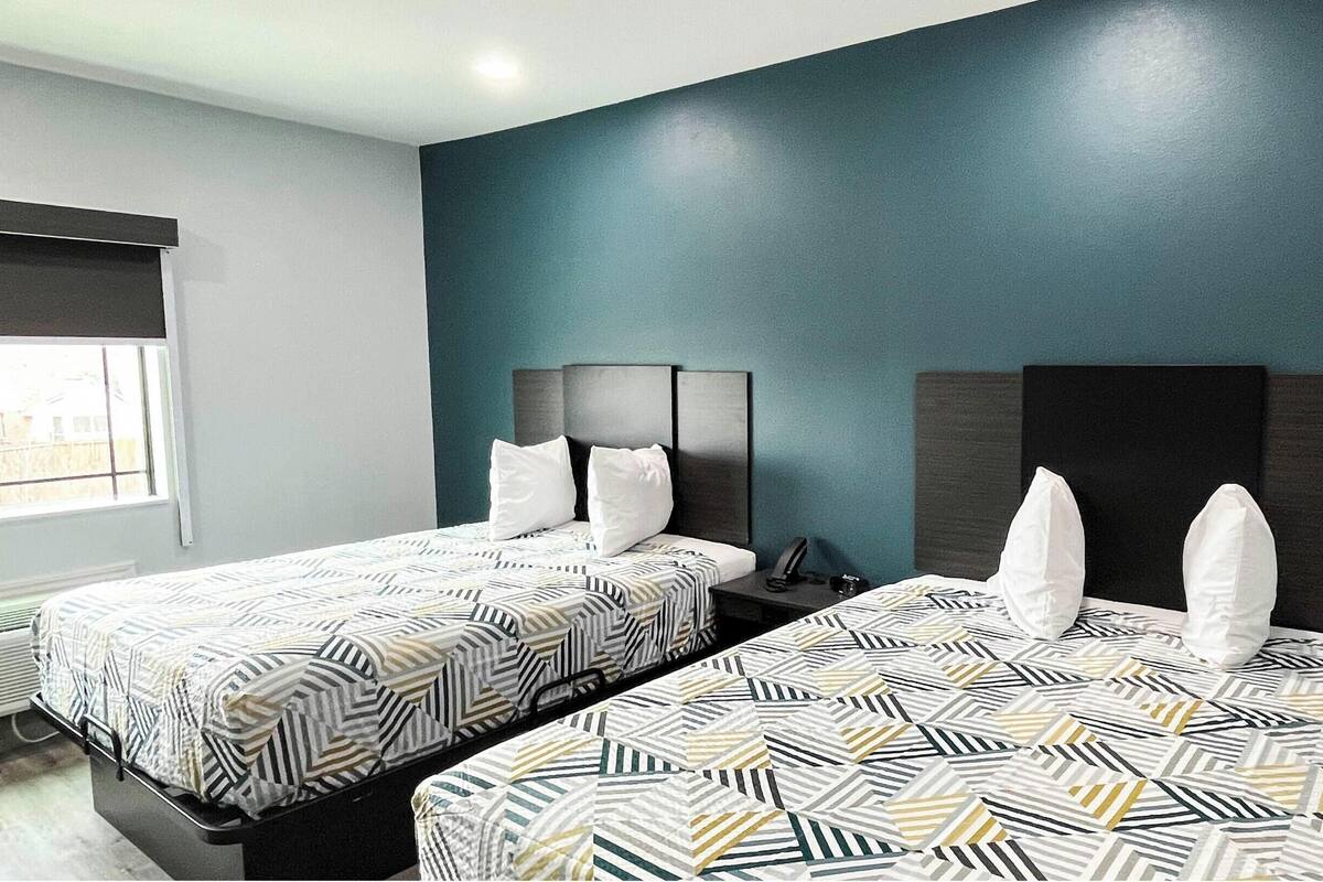 Habitación de hotel con dos camas, cada una con ropa de cama estampada y almohadas blancas, frente a una pared color turquesa.